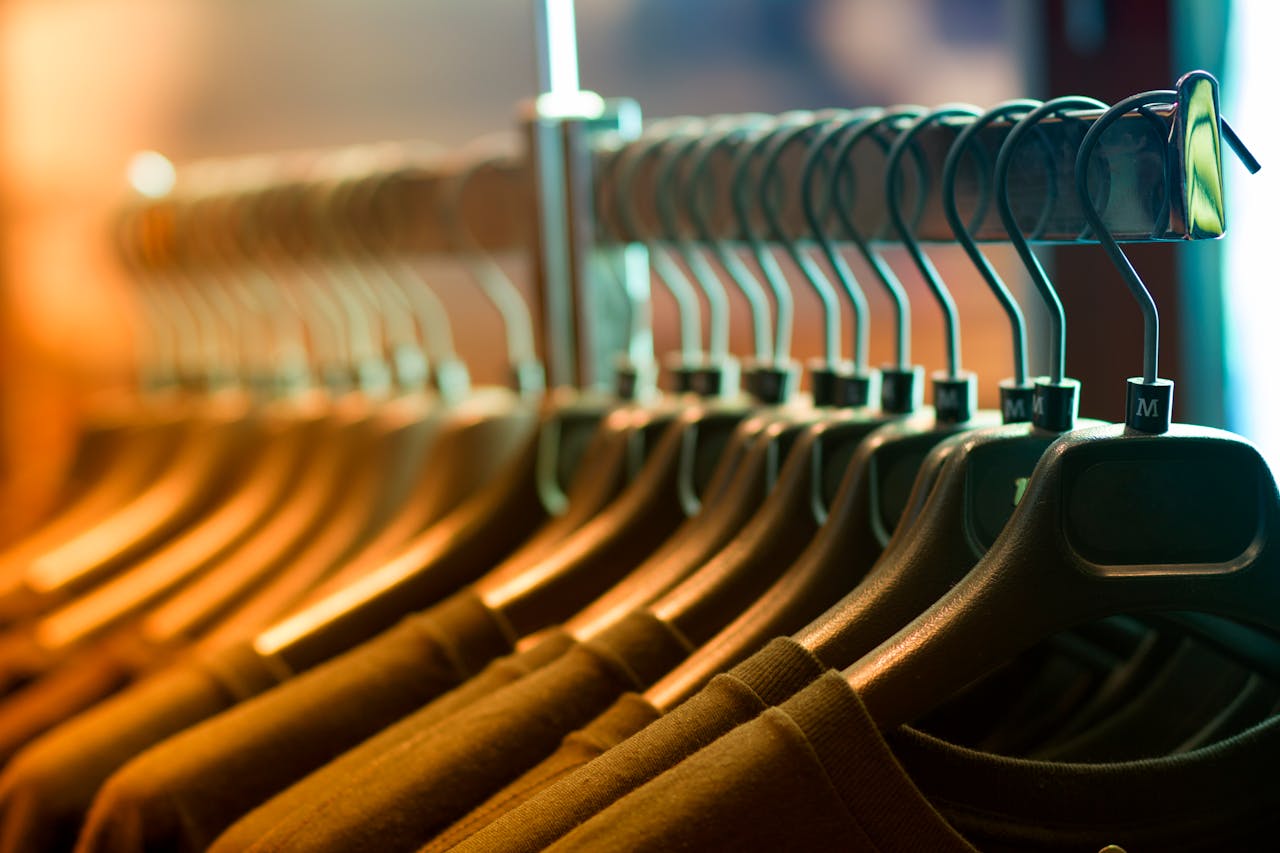 A row of neatly arranged clothes hanging on a rack with wooden hangers.